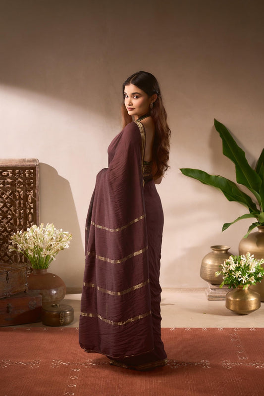 Woman in a purple saree standing in a room with decorative elements.