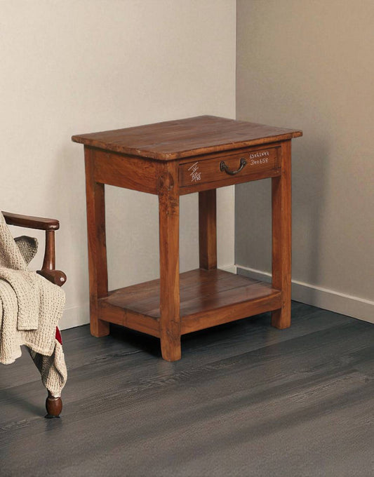 Wooden side table with a drawer next to a chair on a gray floor.