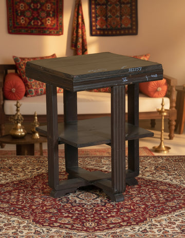 Wooden side table with two shelves on a textured floor and white wall background