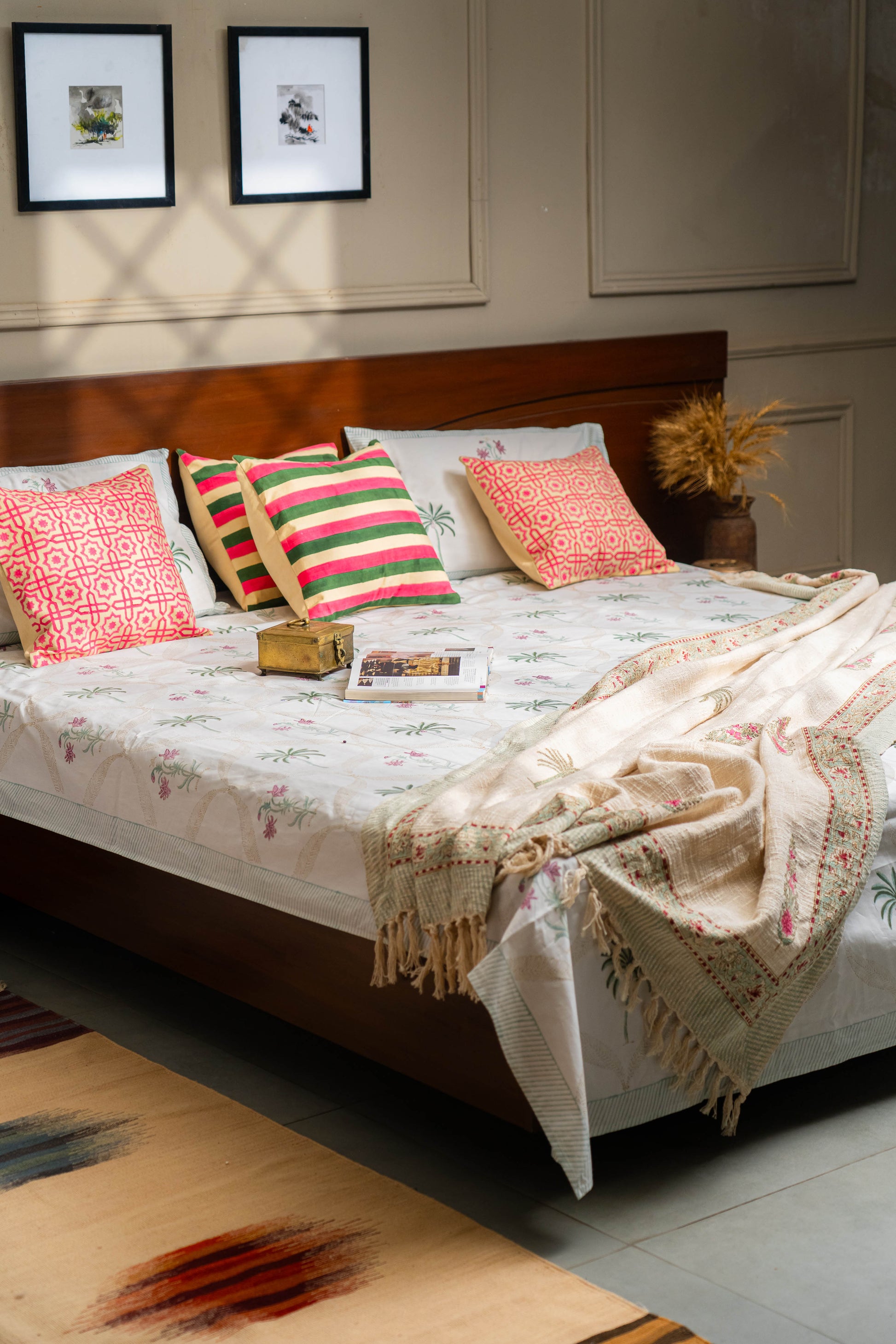 Bedroom with a bed featuring colorful pillows and a blanket, with two framed pictures on the wall.