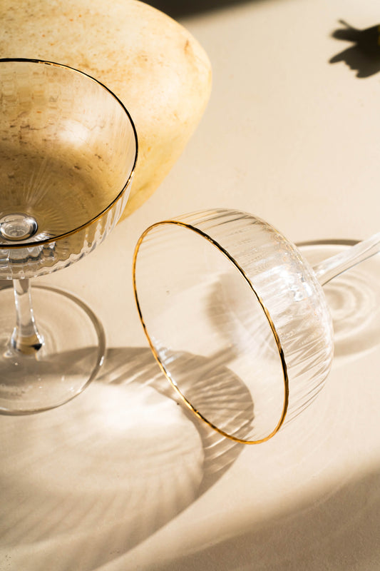 Two gold-rimmed cocktail glasses on a light surface