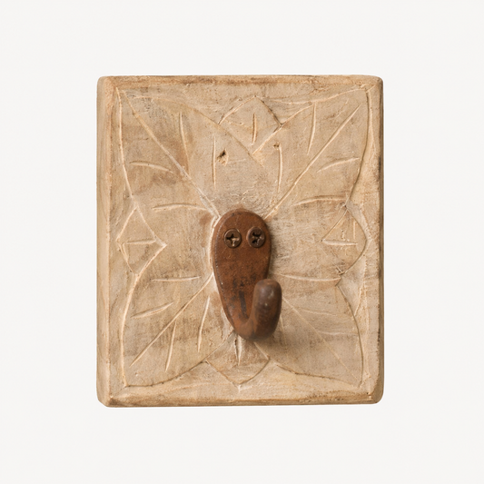 A rustic, square carved wooden wall hook with a textured leaf pattern and a central brown metal hook, shown against a plain white background.