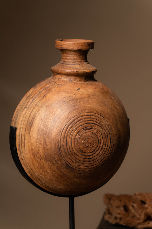 Complementing the beauty of the clay pot is the intricately designed iron stand, adding an element of rustic charm and stability.