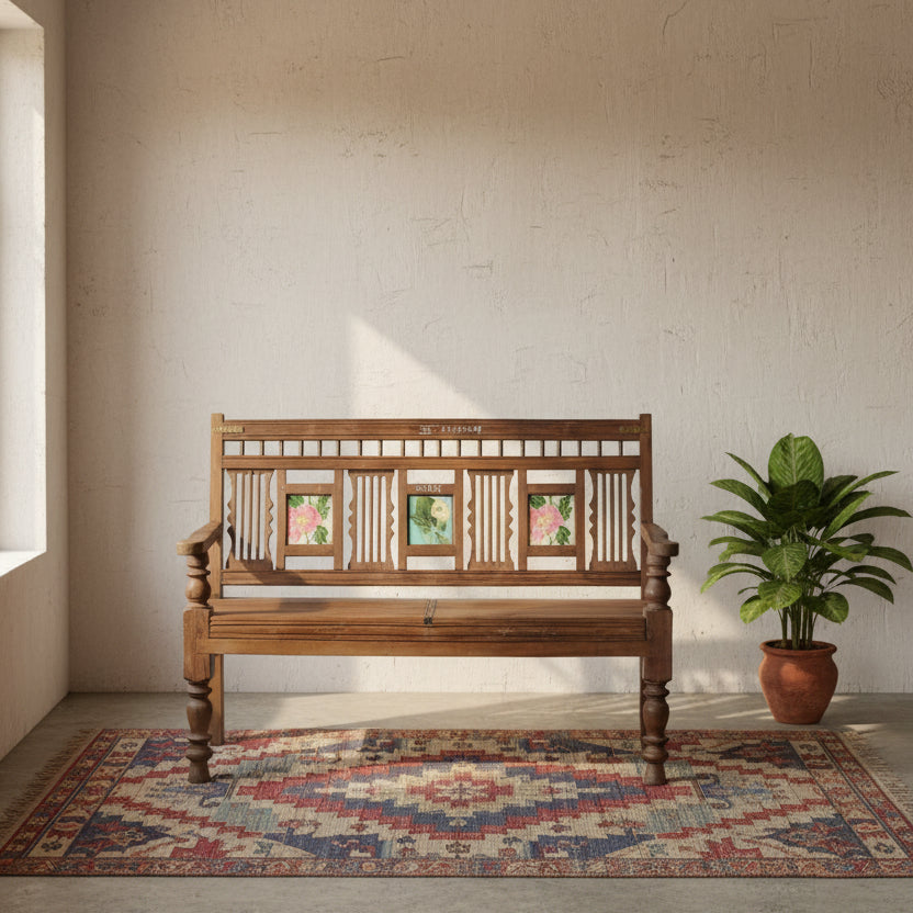 A rustic dark brown wooden bench with carved details and three colorful floral inlays on the backrest, set against a gray cinderblock wall.