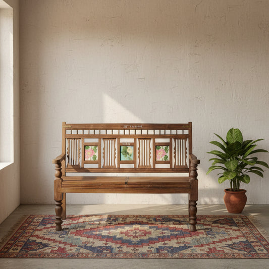 A rustic dark brown wooden bench with carved details and three colorful floral inlays on the backrest, set against a gray cinderblock wall.