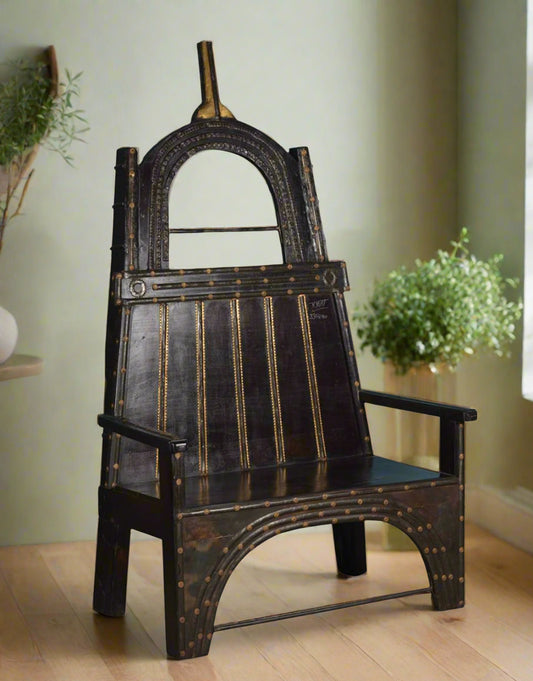 Handcrafted from premium teak wood, the high-back silhouette features an arched iron frame adorned with brass accents and rivets, lending it both strength and stately grace.