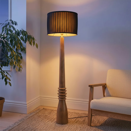 Floor lamp with a black shade in a room with a plant and a chair.