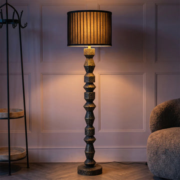 Decorative floor lamp with a textured base and black shade in a room setting.