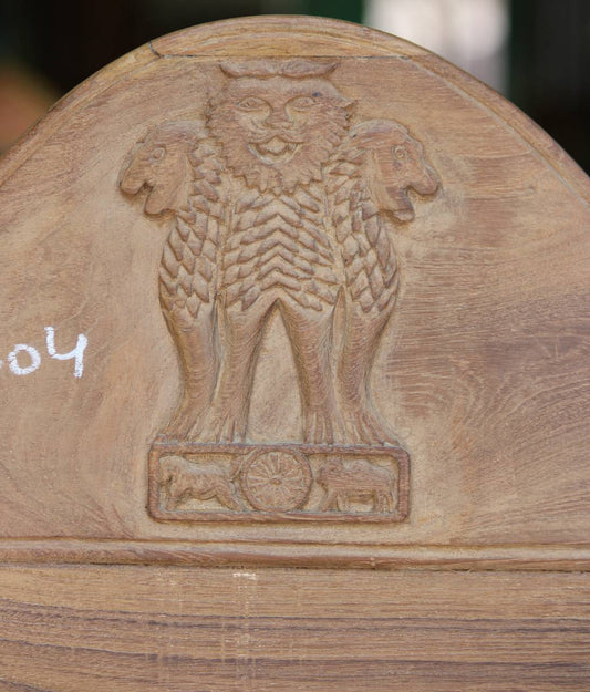 Wooden chair with a carved emblem of a lion on a shield, resembling the Indian national emblem.