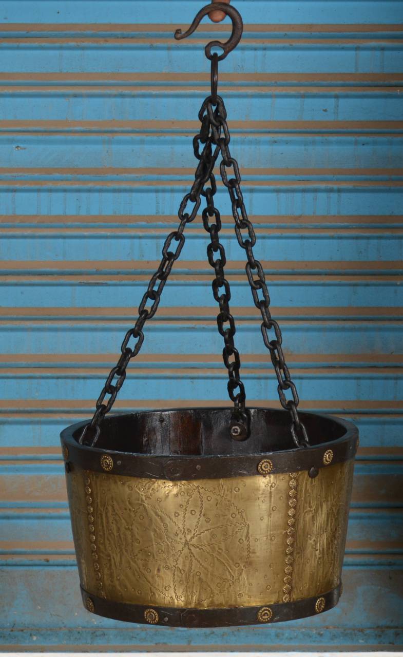 Made from rich teak wood, adorned with detailed embossed brass panels, and suspended by sturdy iron chains, this unique planter adds a regal and rustic touch to any space.