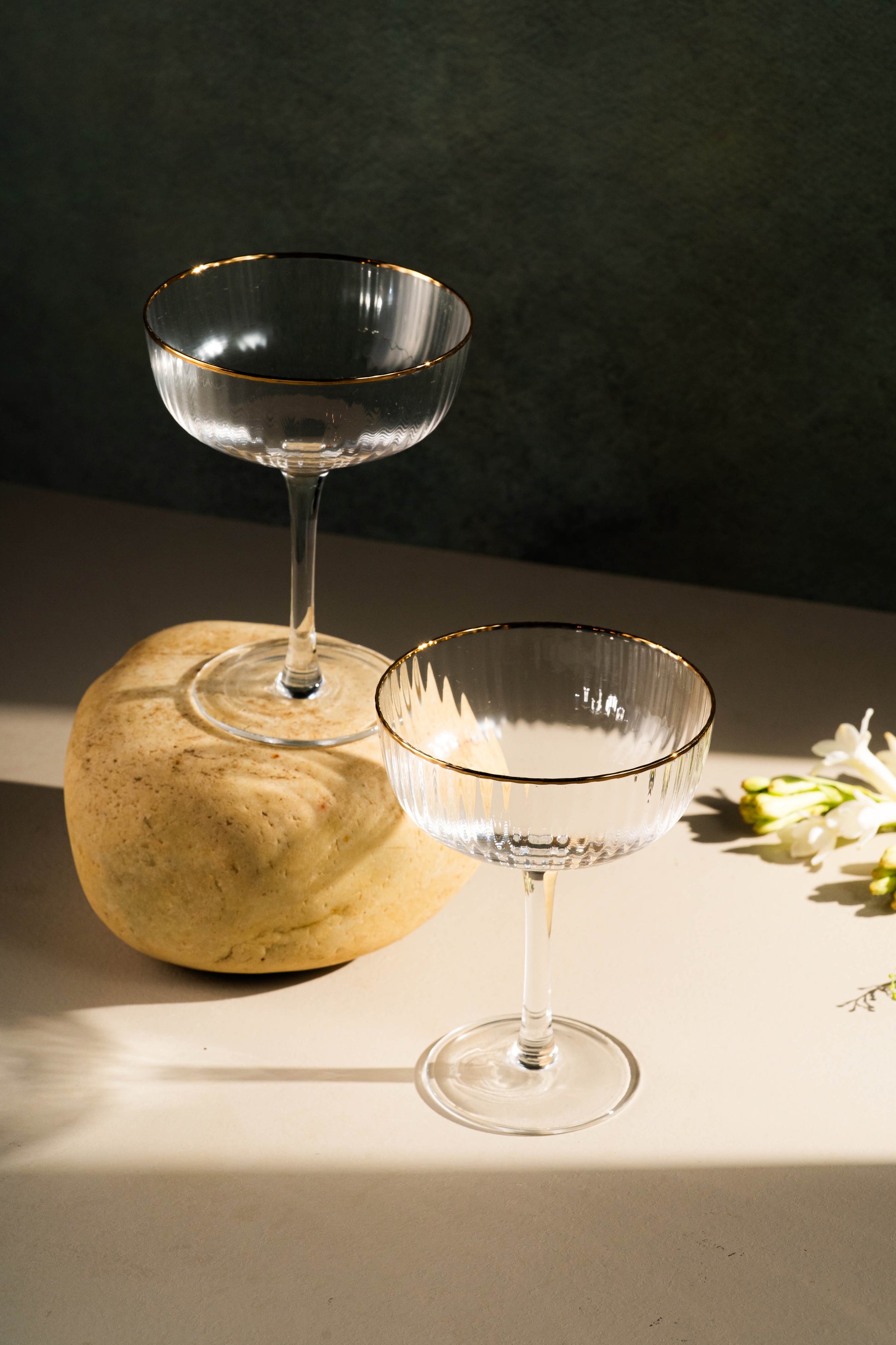 Two clear glass cocktail glasses on a light surface with a dark background