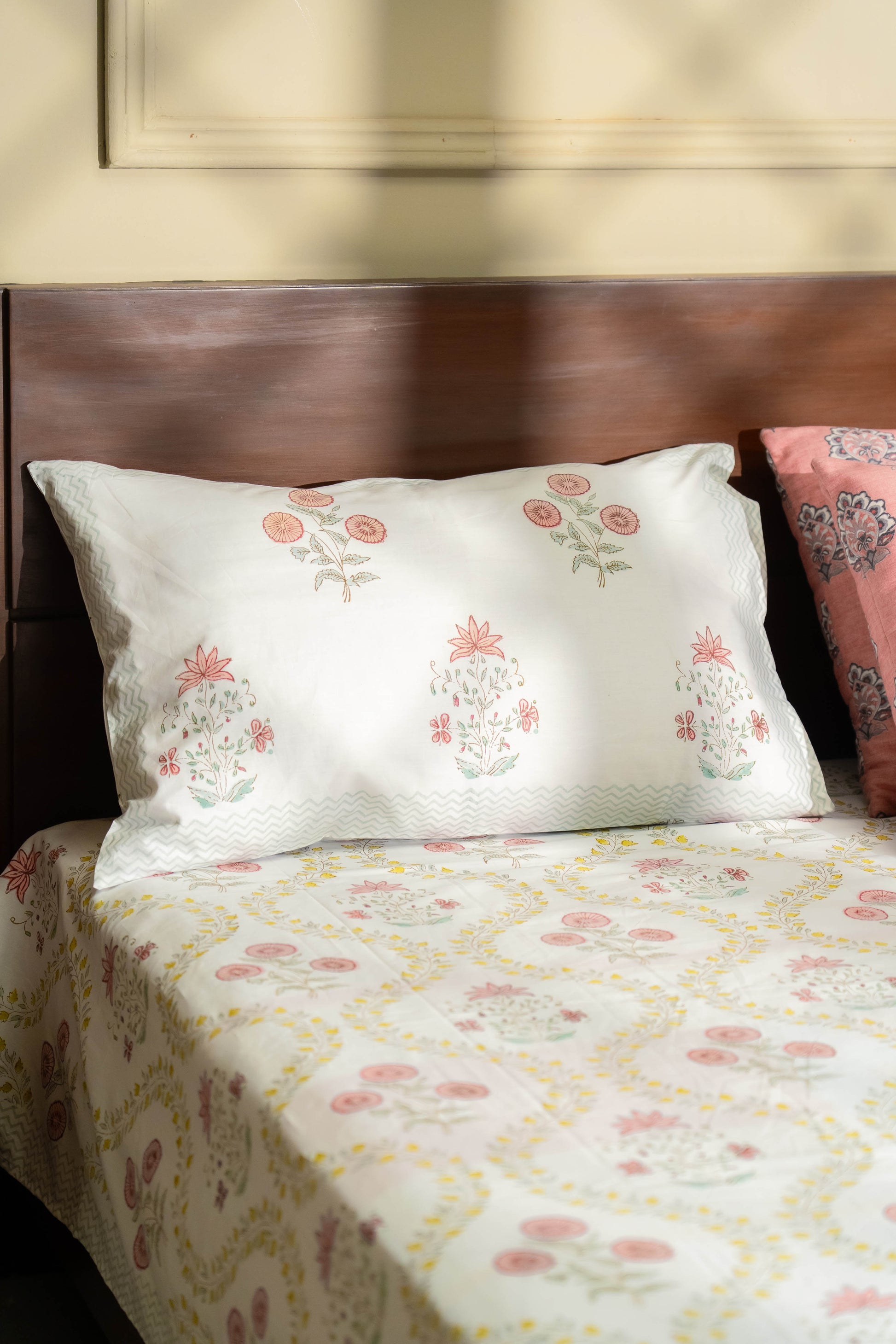 Floral-patterned bedspread and pillows on a bed with a wooden headboard.