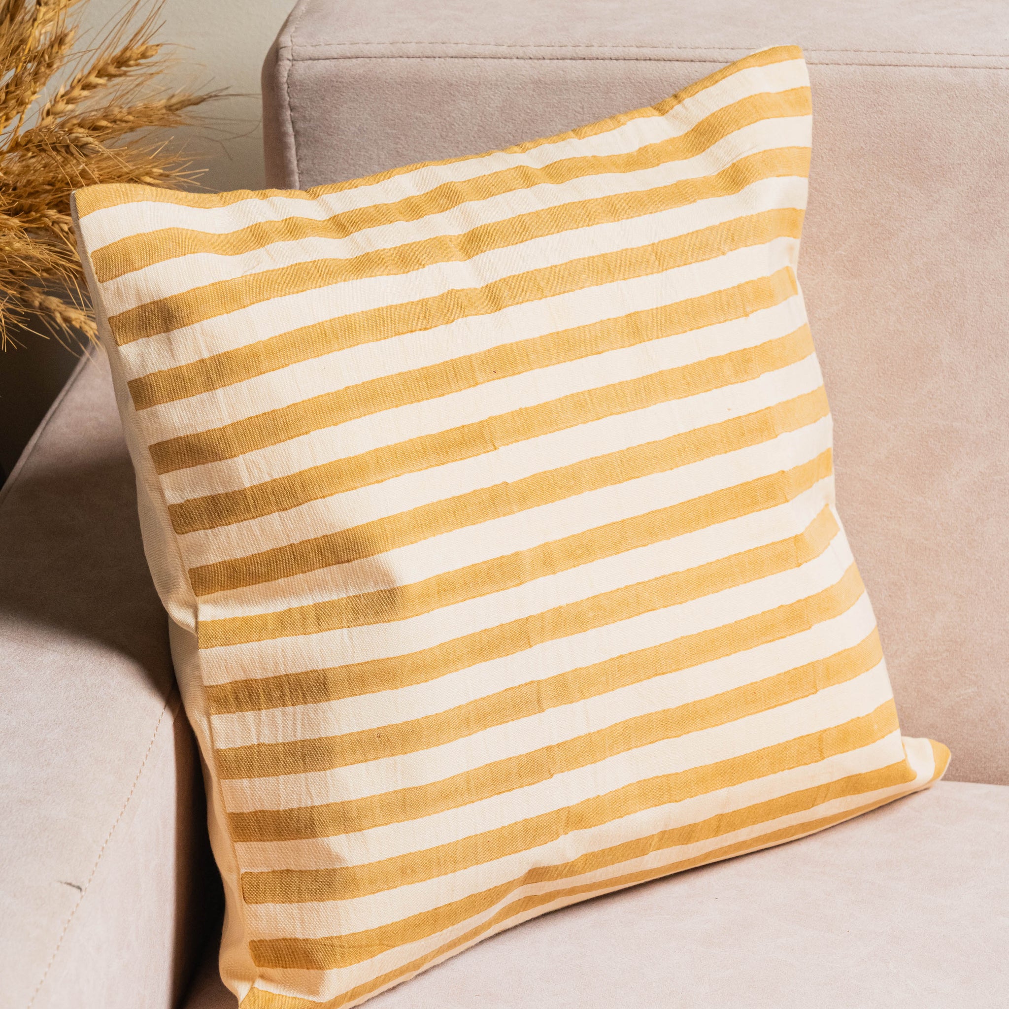 Yellow and white striped pillow on a beige sofa with a neutral background