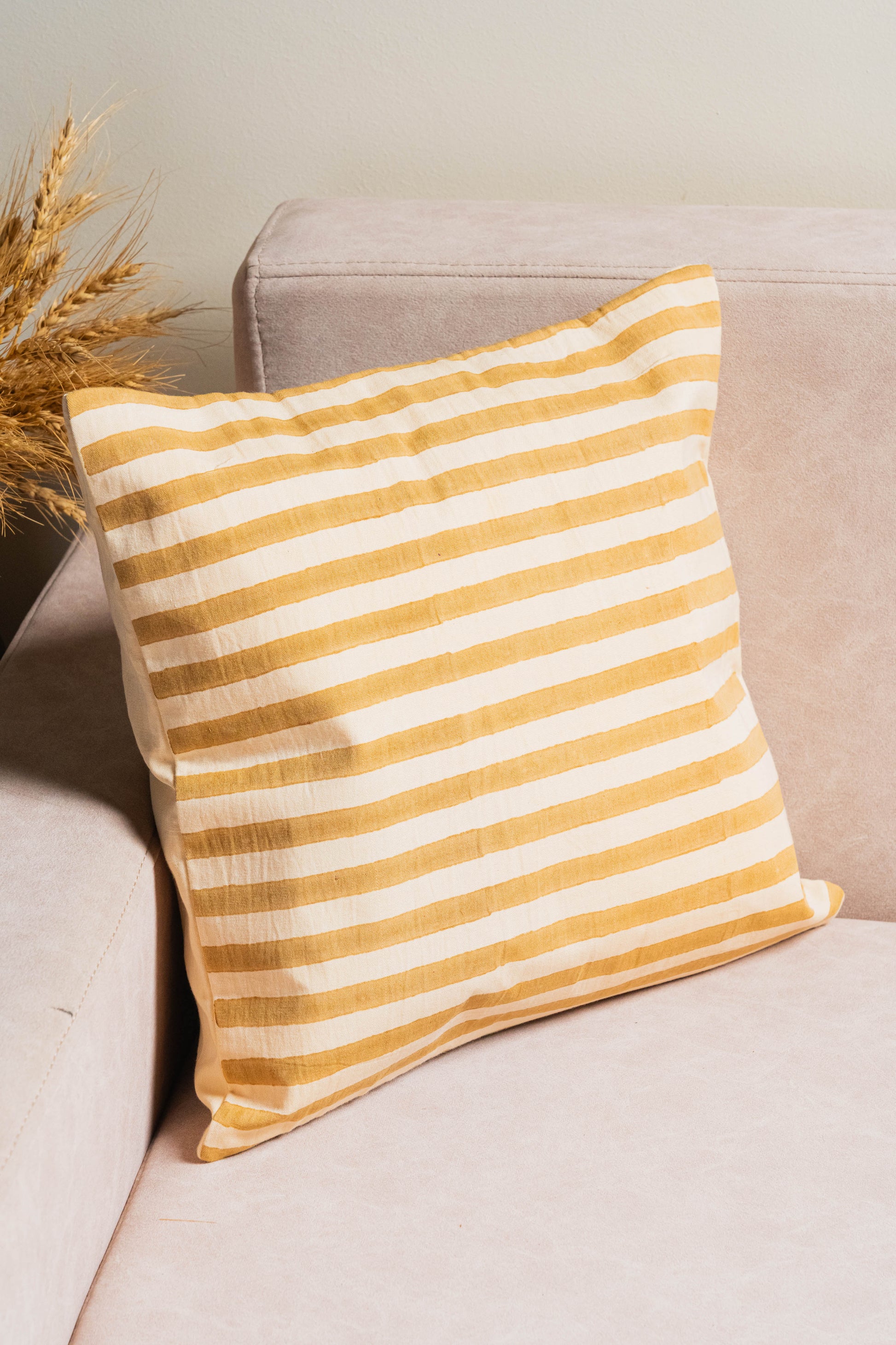 Yellow and white striped pillow on a beige sofa with a neutral background