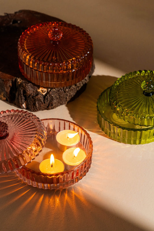 Three glass candle holders in red, clear, and green with floating candles on a reflective surface.