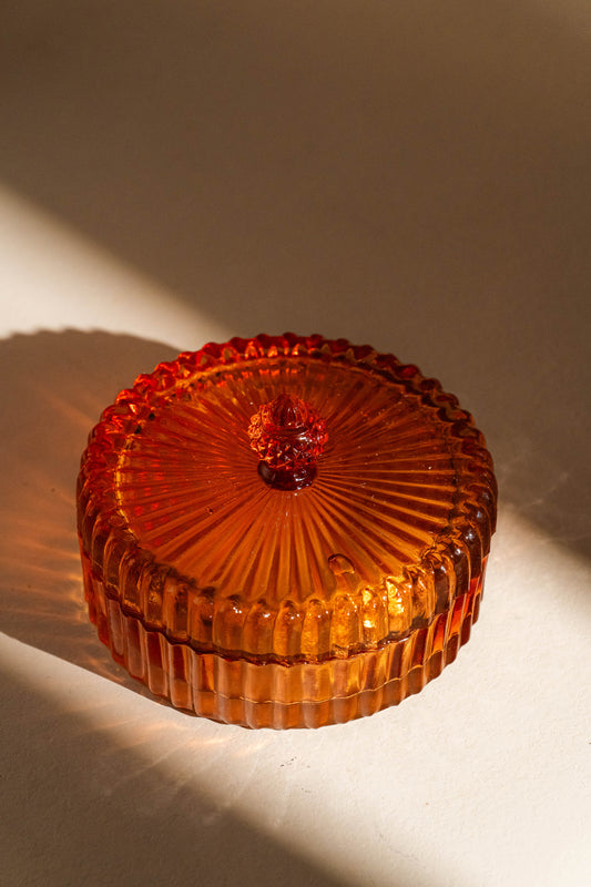 Amber glass trinket box with lid on a beige background