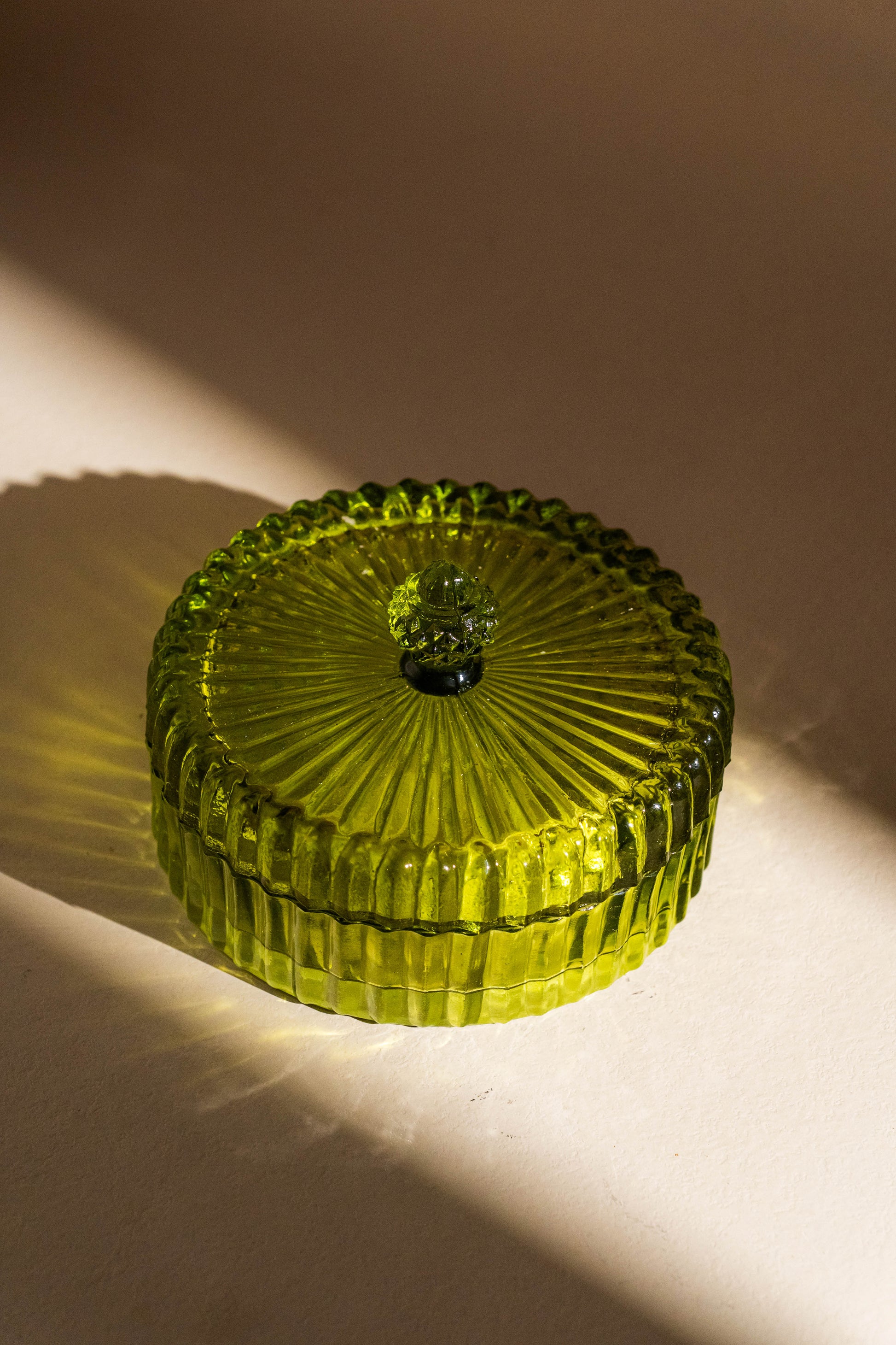 Green glass container with a textured lid on a beige background