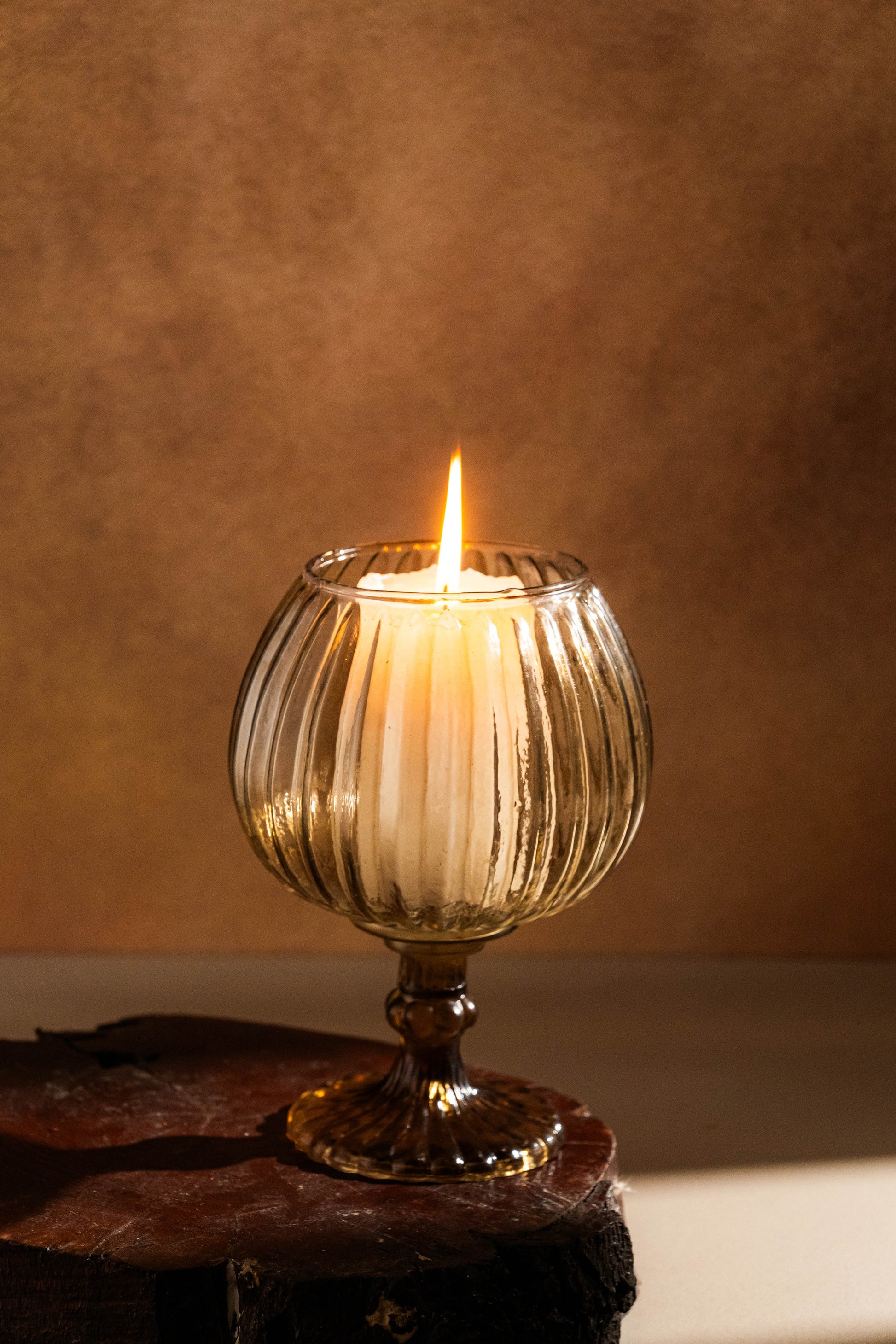 Candle in a ribbed glass holder on a wooden surface with a warm brown background