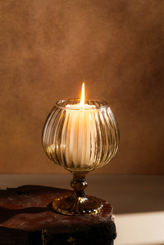 Candle in a ribbed glass holder on a wooden surface with a warm brown background