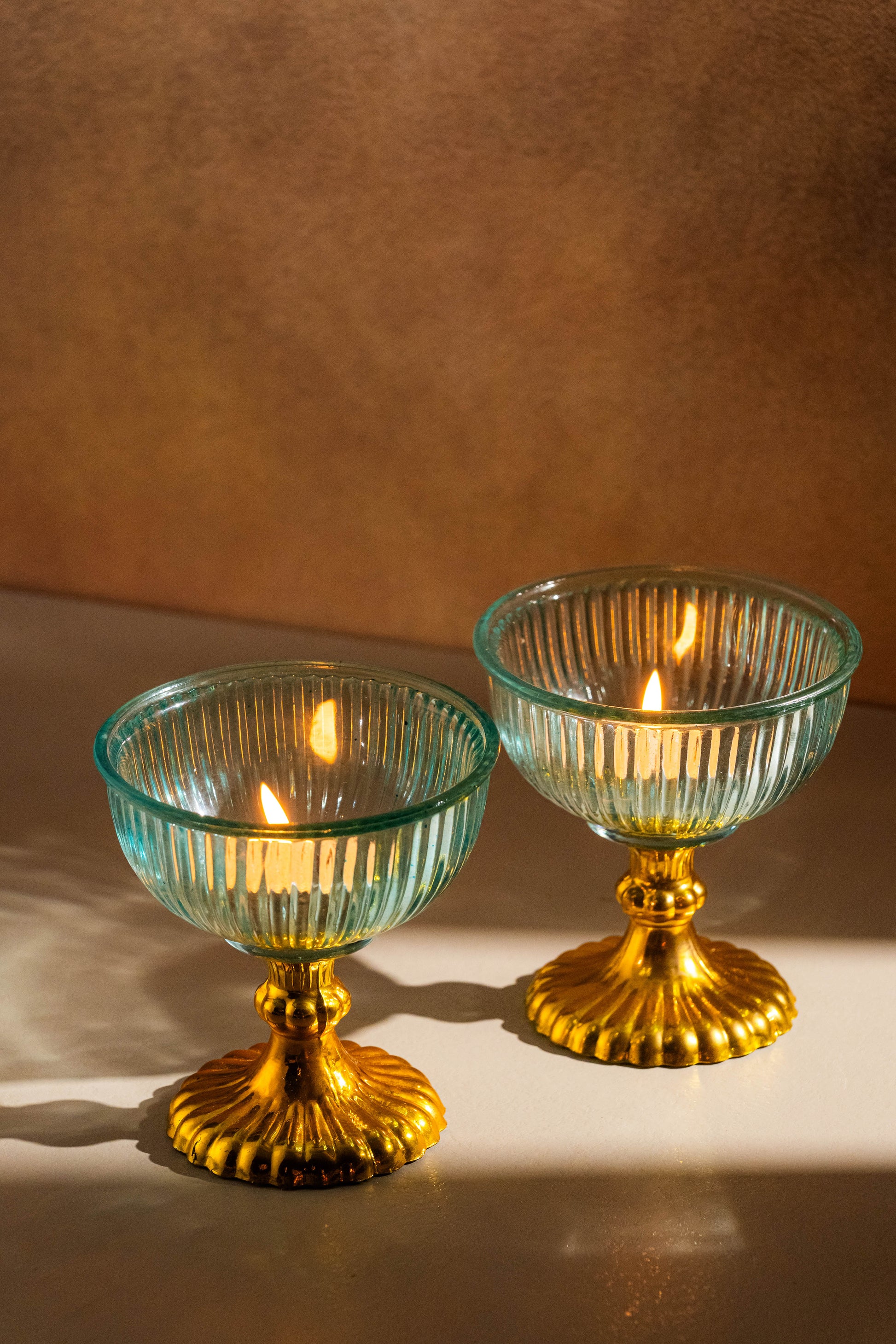 Two glass candle holders with gold bases on a brown background
