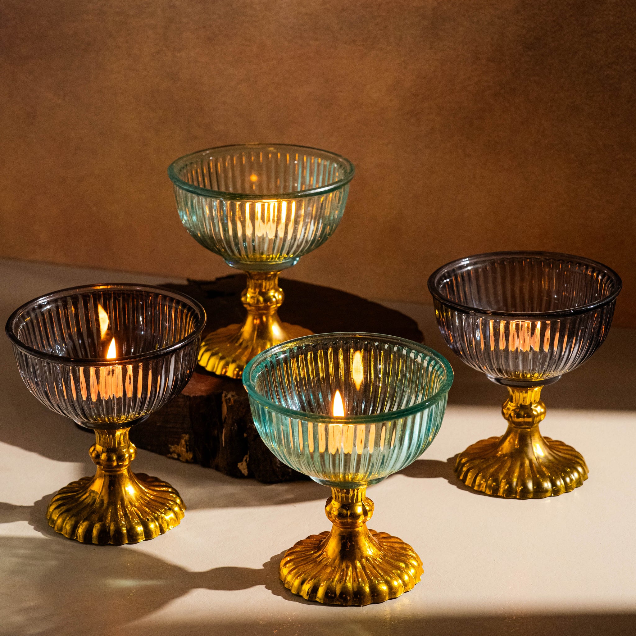 Set of four glass candle holders with gold bases on a brown background