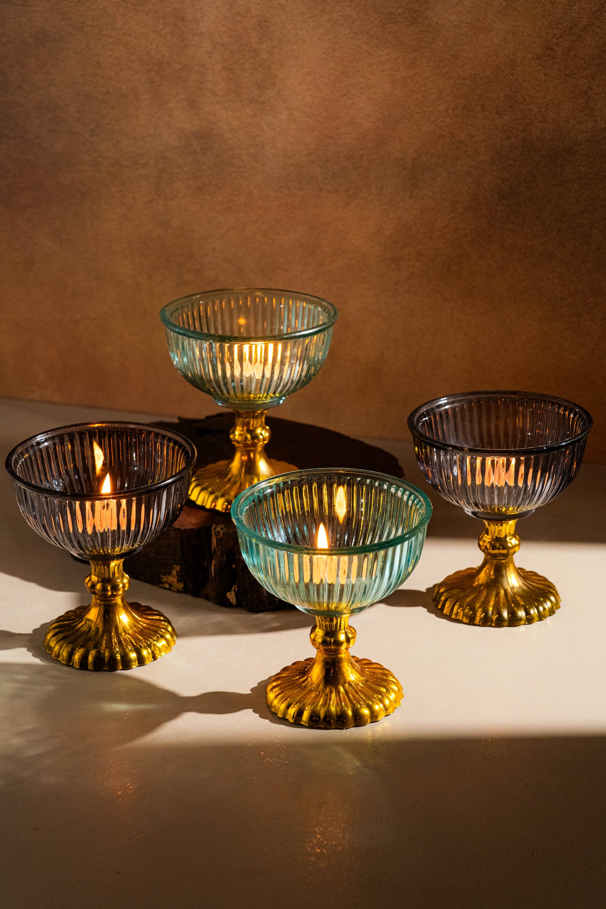 Set of four glass candle holders with gold bases on a brown background