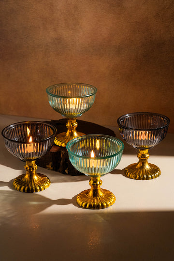Set of four glass candle holders with gold bases on a brown background