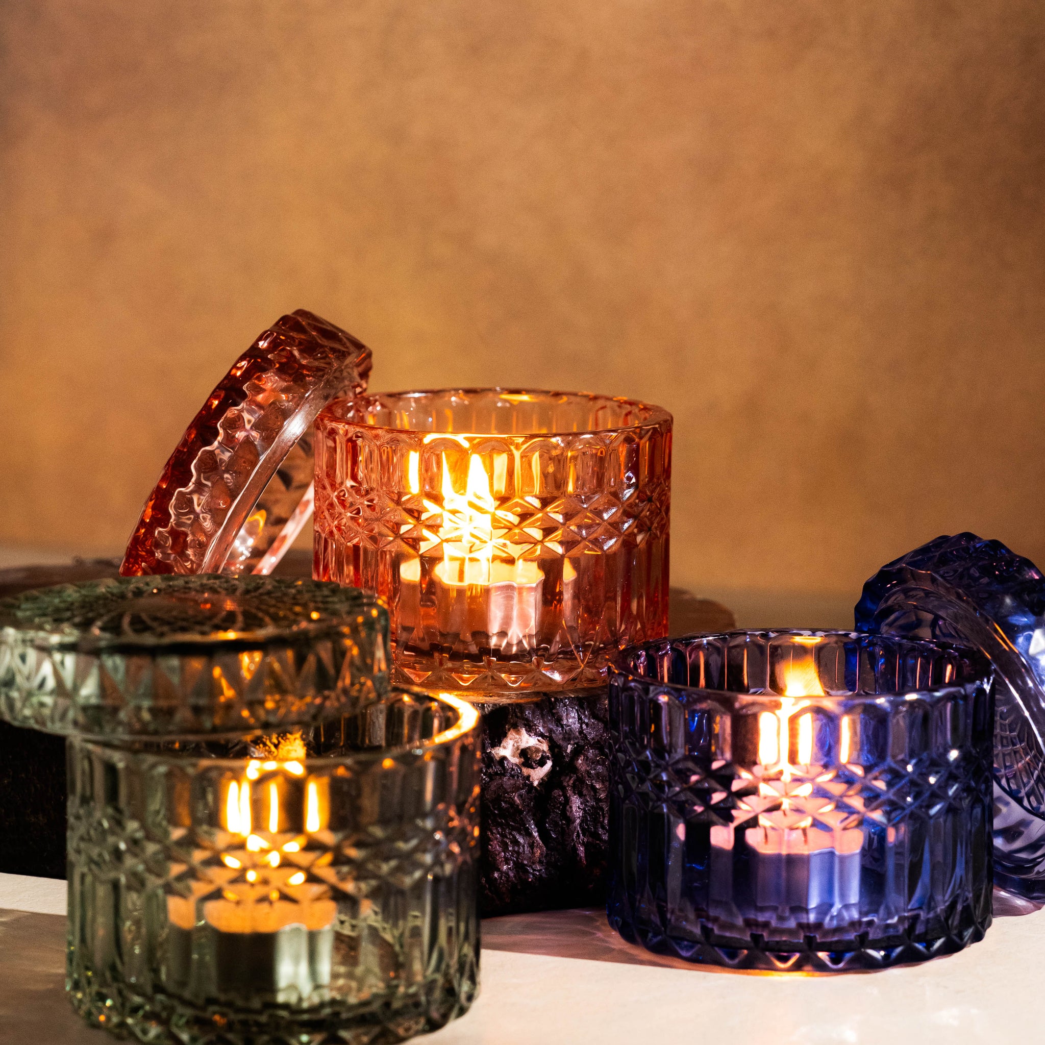 Set of colorful glass candle holders with lit candles on a reflective surface.