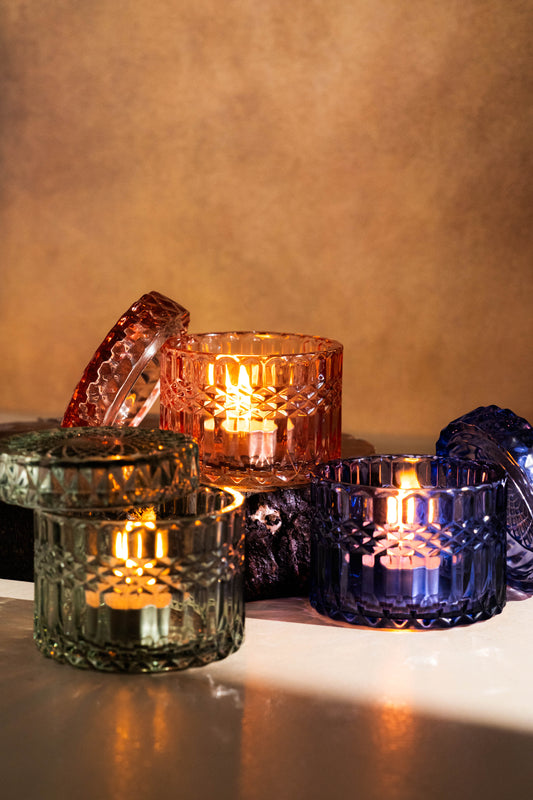 Set of colorful glass candle holders with lit candles on a reflective surface.