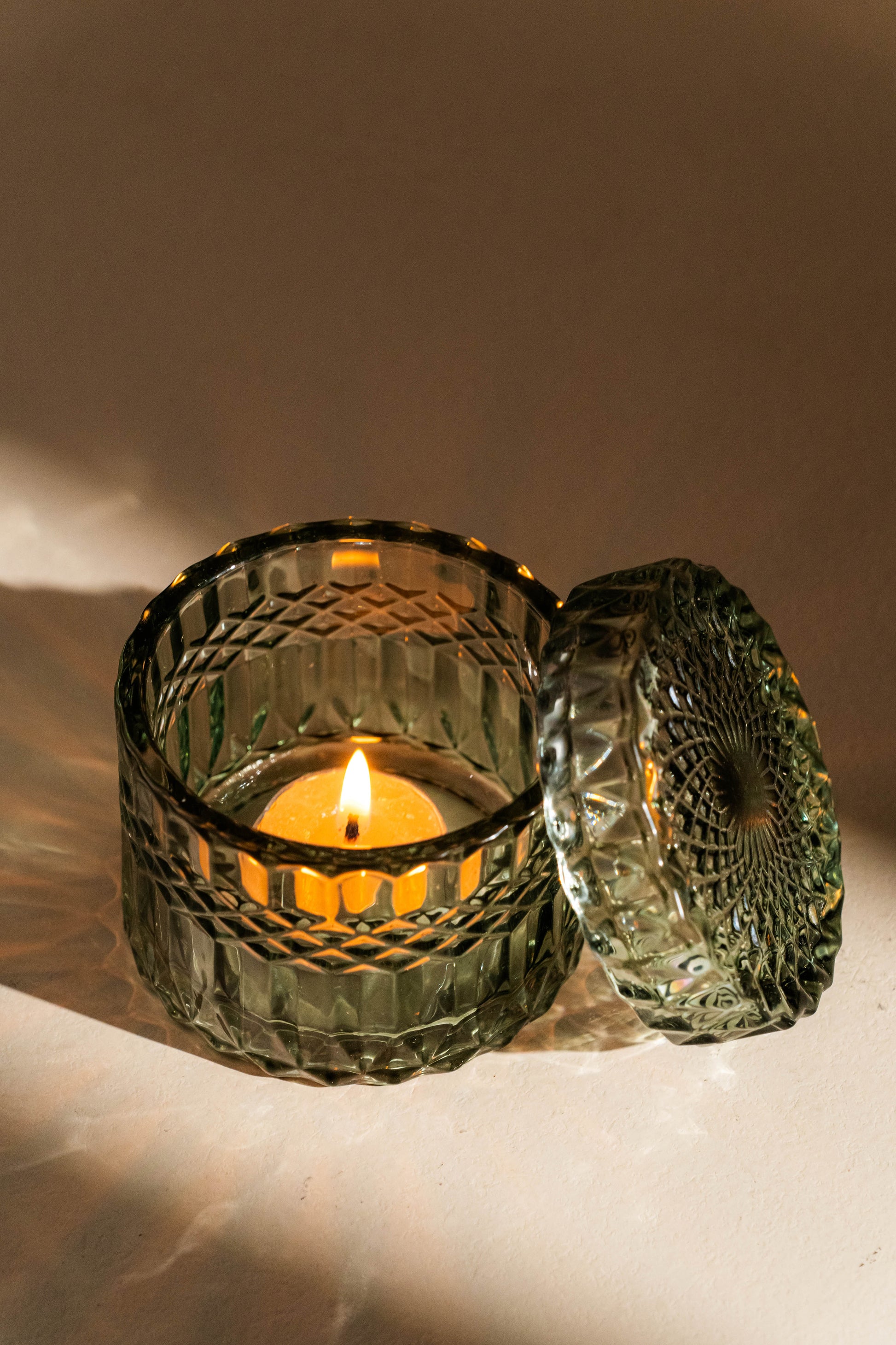 Decorative glass candle holder with a lit candle on a neutral background