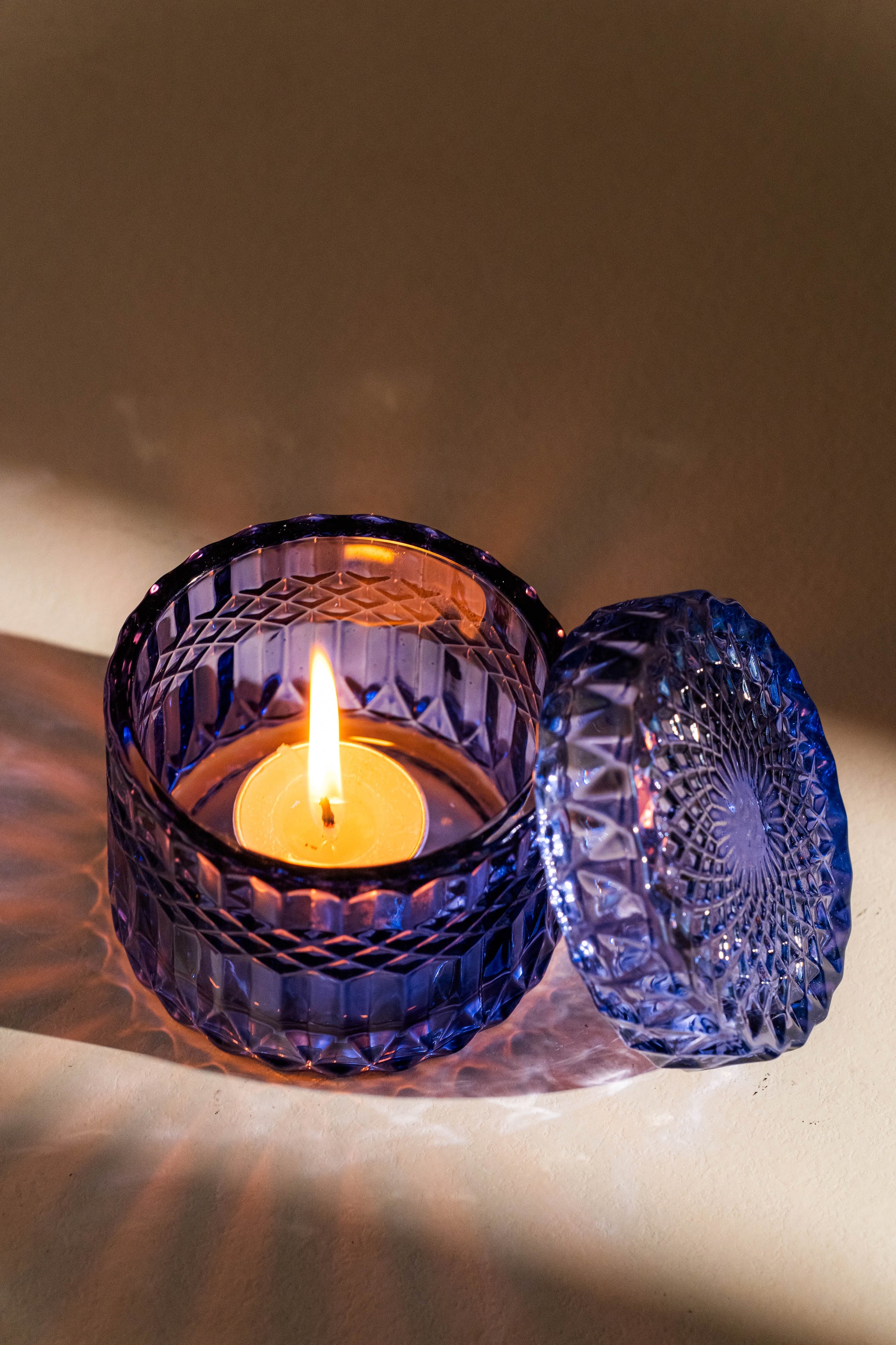 Blue glass candle holder with a lit candle on a neutral background