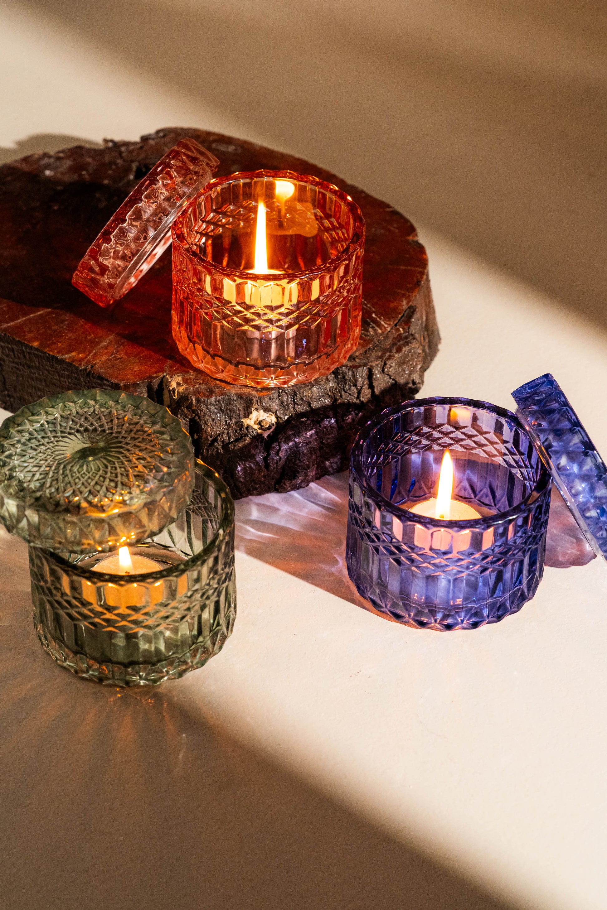 Colorful glass candle holders with lit candles on a wooden surface