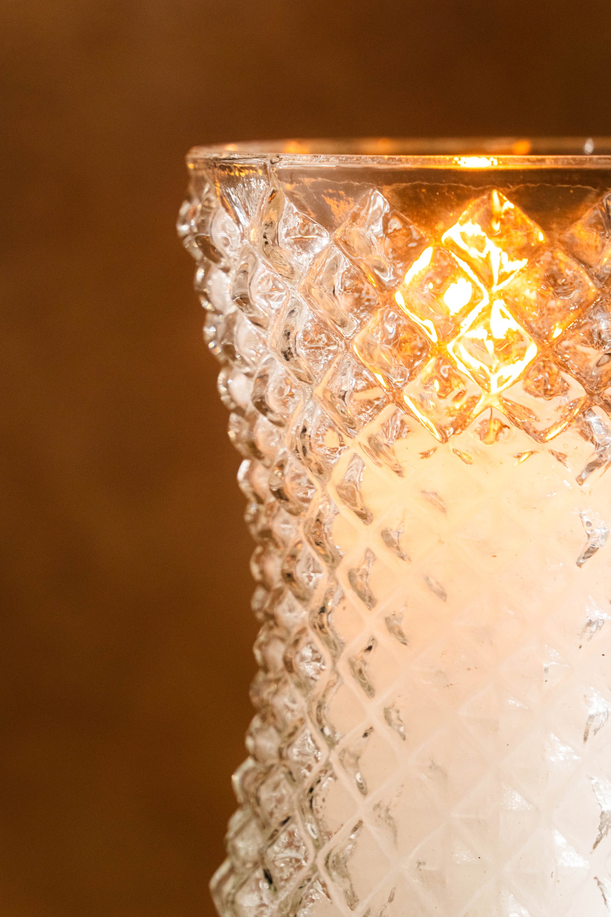 Decorative glass candle holder with textured surface and warm glow against a dark background