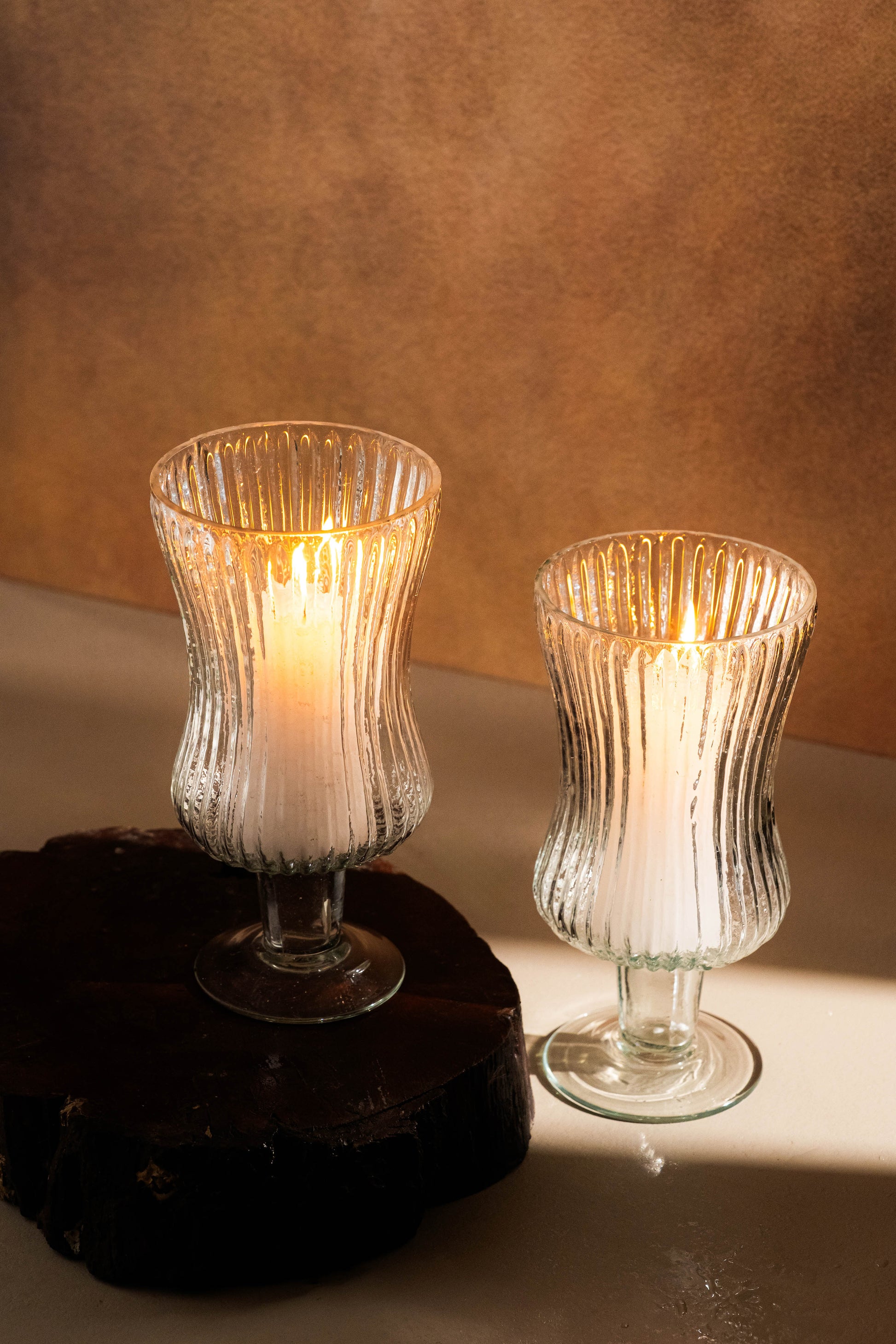 Two glass candle holders with lit candles on a textured surface.