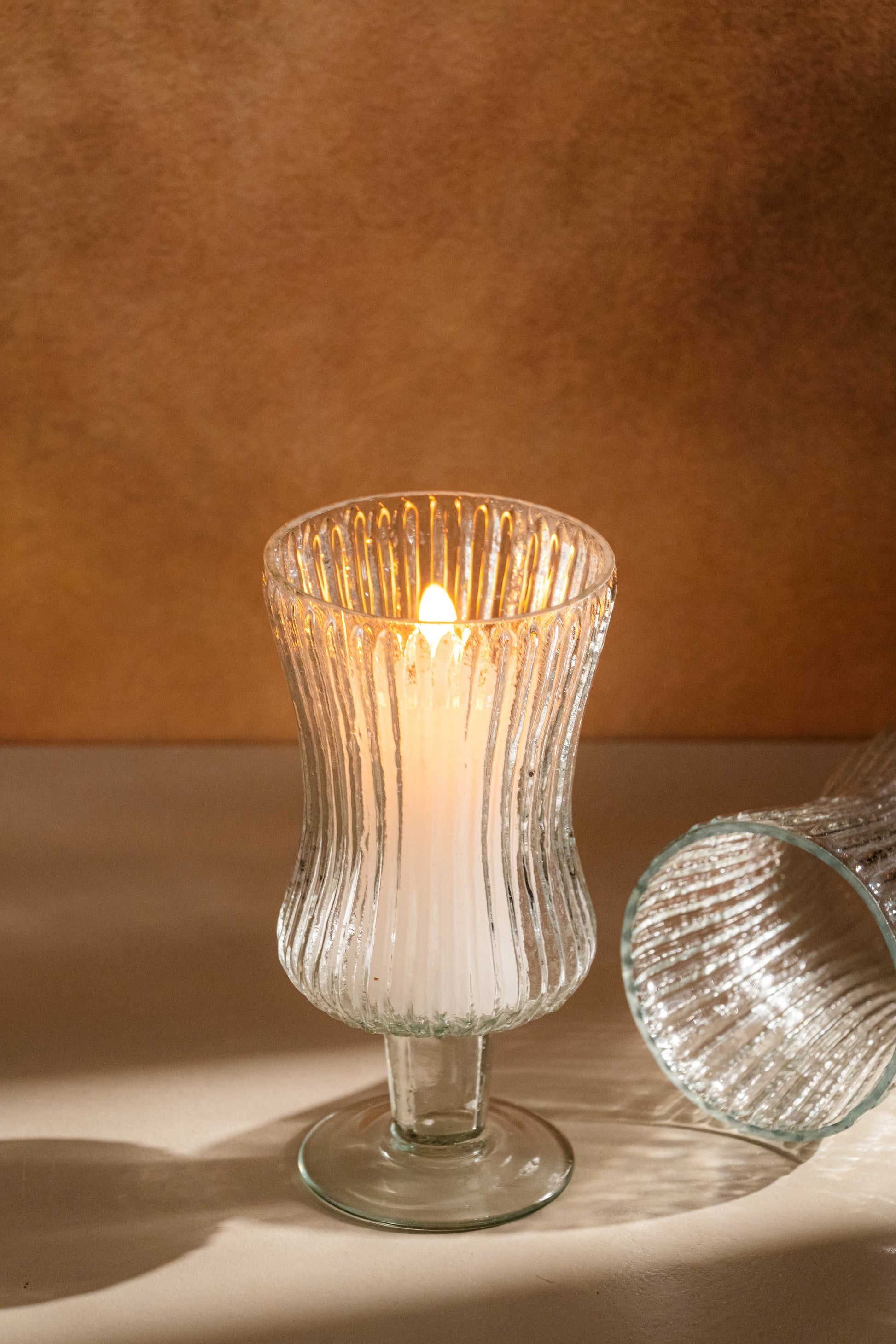 Glass candle holder with a lit candle on a brown background
