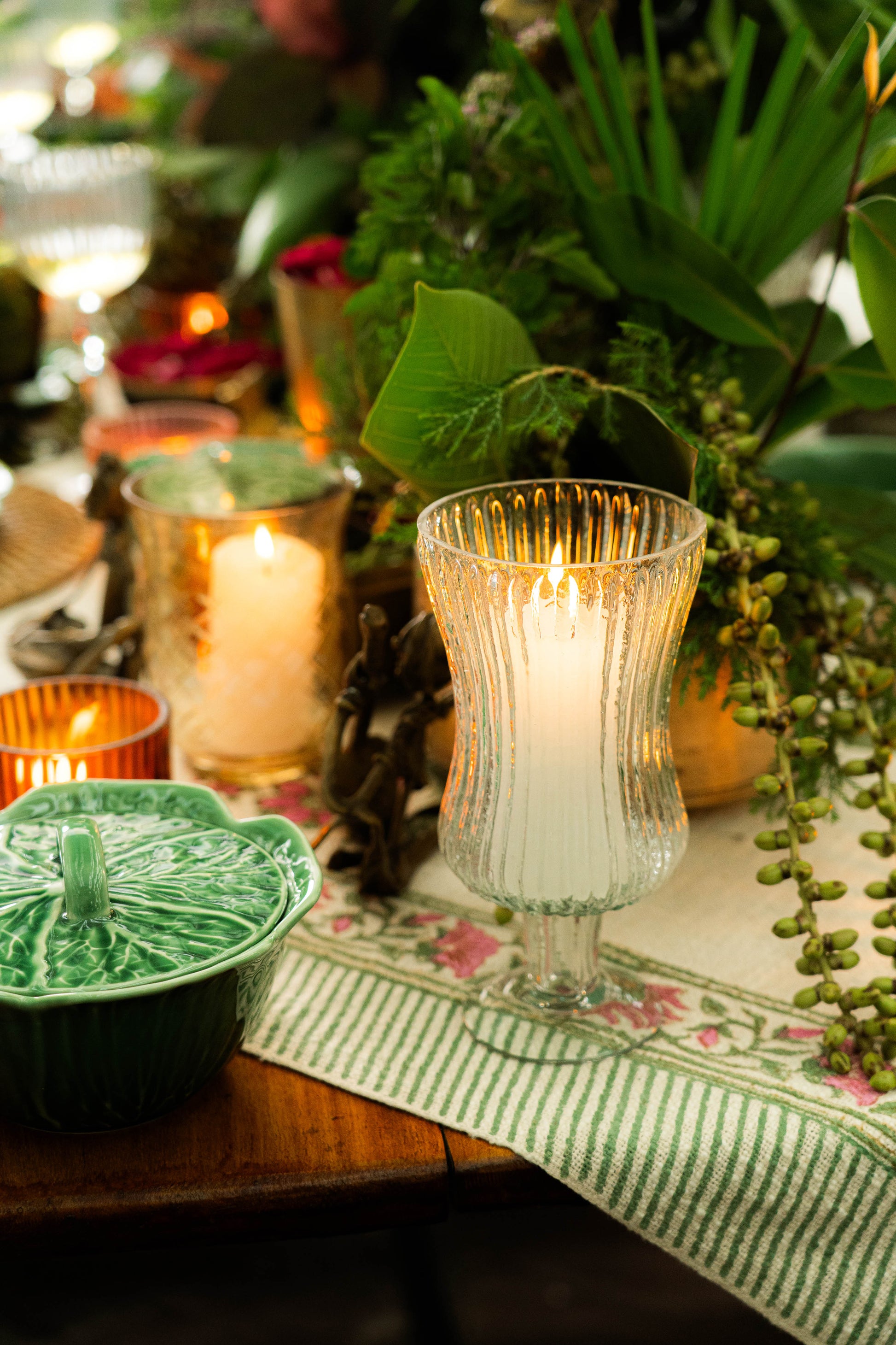 Candlelit table setting with greenery and decorative items on a floral tablecloth.