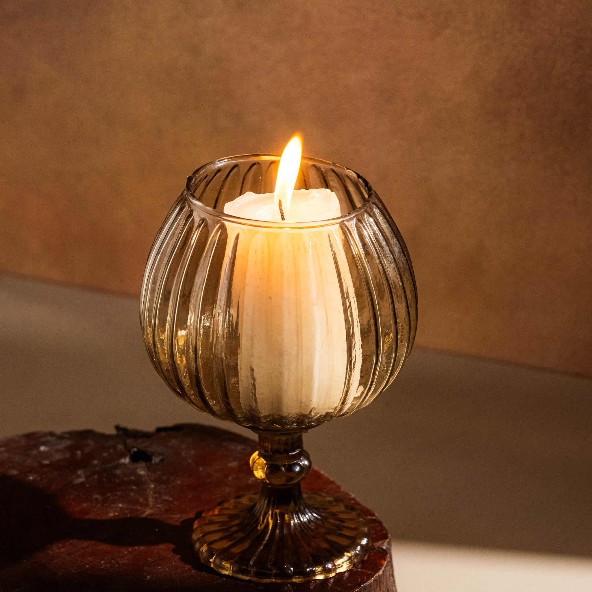 Candle in a decorative glass holder on a wooden surface with a warm background