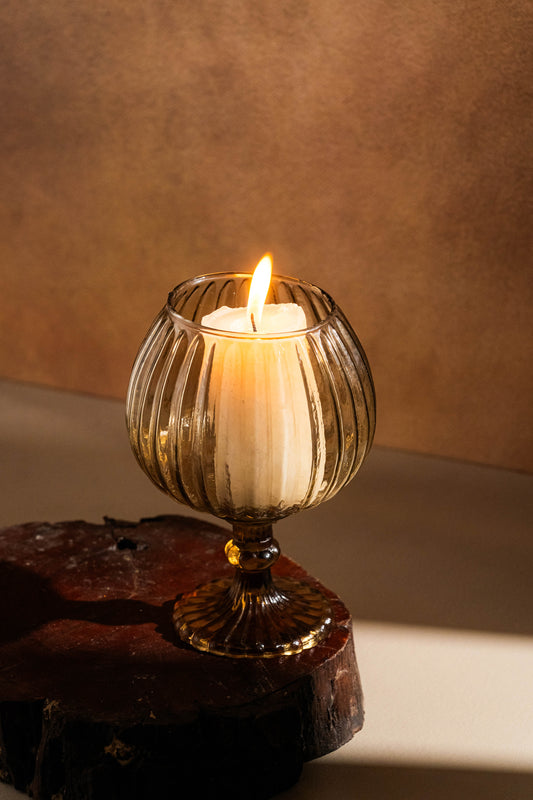Candle in a decorative glass holder on a wooden surface with a warm background
