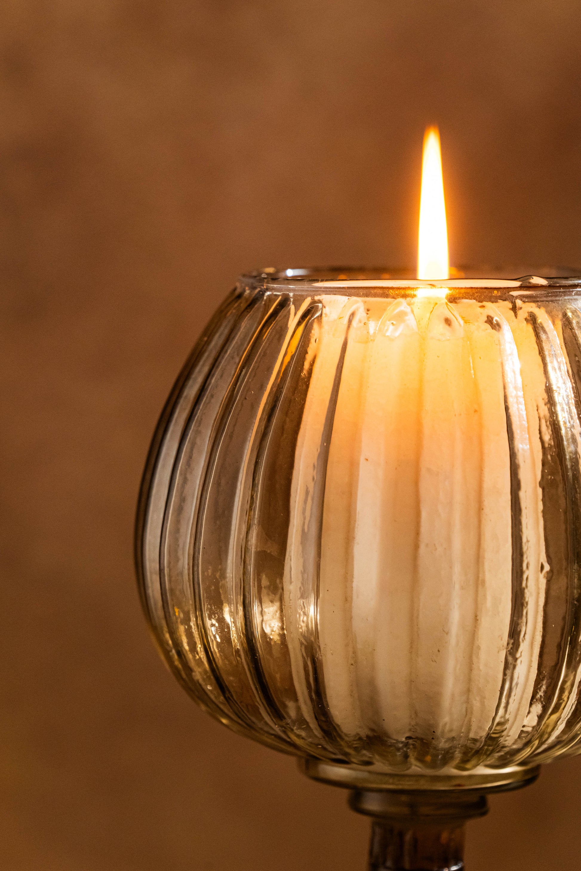 Candle in a ribbed glass holder with a warm glow against a brown background
