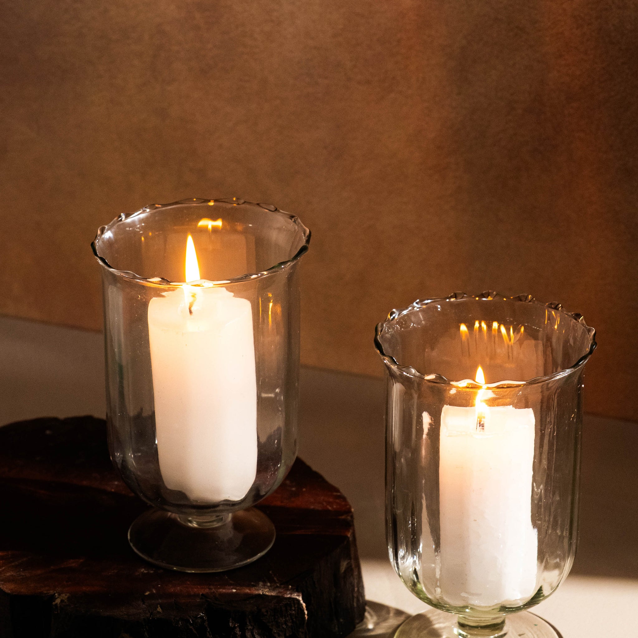 Two white candles in glass holders on a wooden surface with a brown background