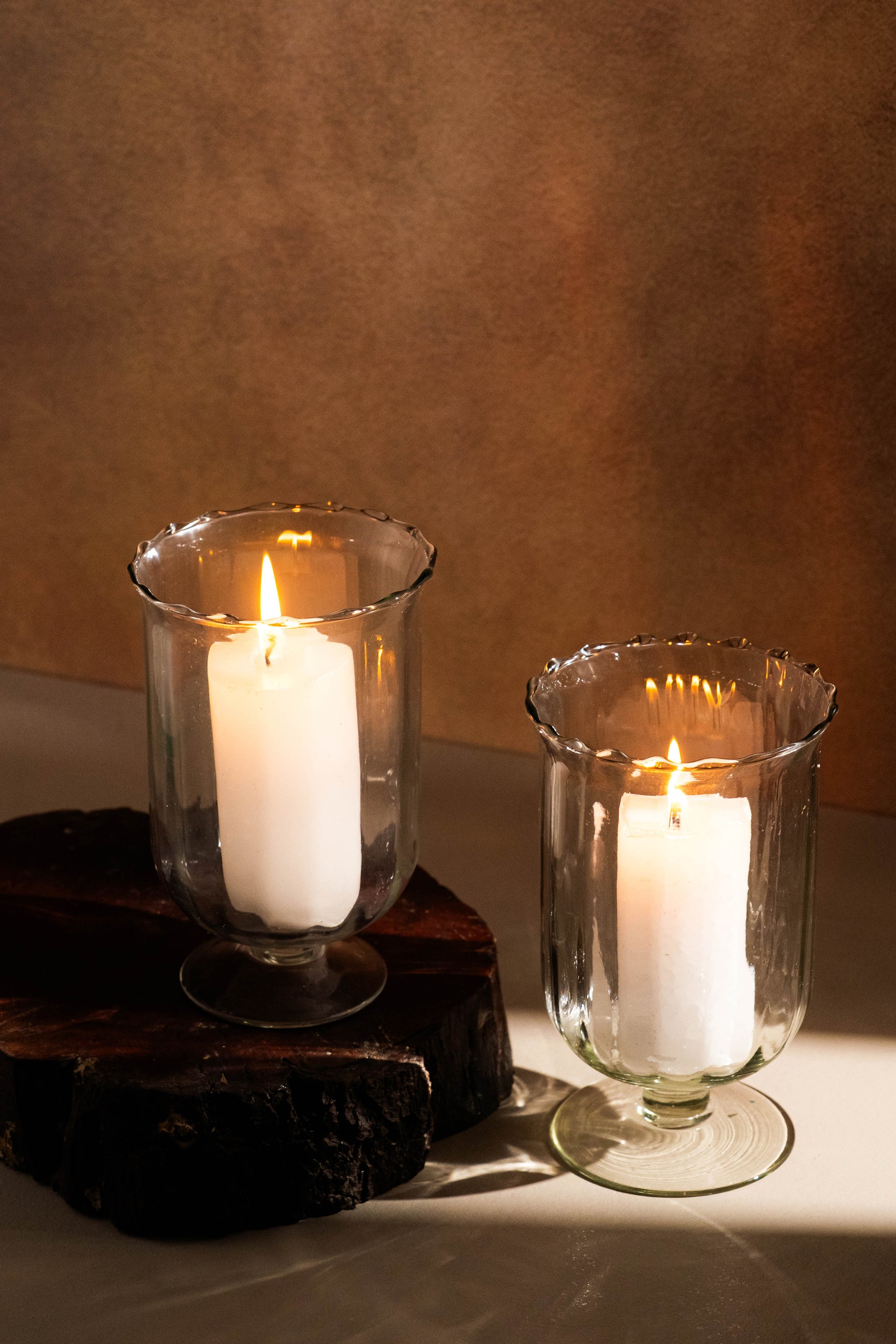 Two white candles in glass holders on a wooden surface with a brown background
