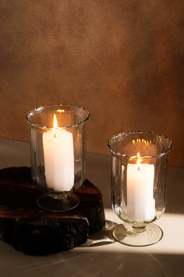 Two white candles in glass holders on a wooden surface with a brown background