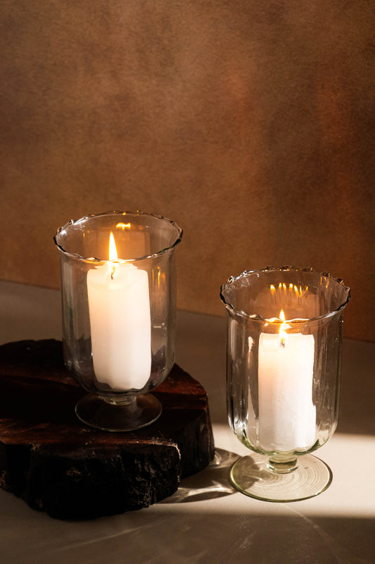Two white candles in glass holders on a wooden surface with a brown background