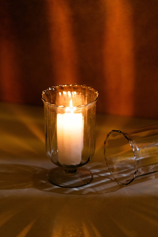 Candle in a glass holder on a reflective surface with a blurred background