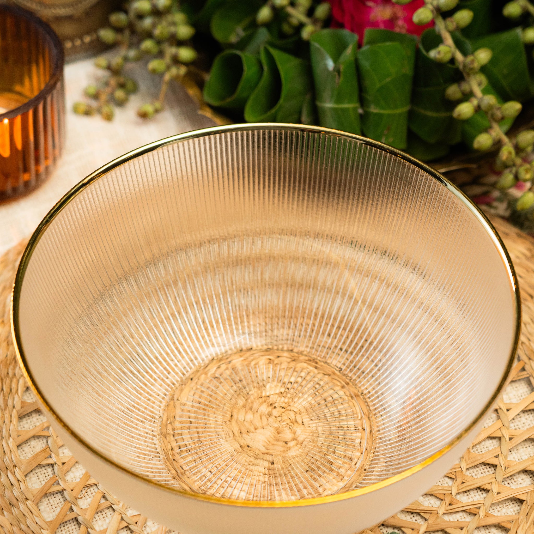 Gold decorative bowl on a woven placemat with greenery and a candle in the background