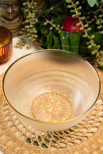 Gold decorative bowl on a woven placemat with greenery and a candle in the background