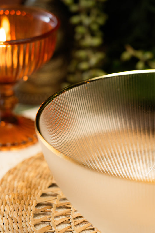 Close-up of a textured gold rimmed glass with a candle in the background