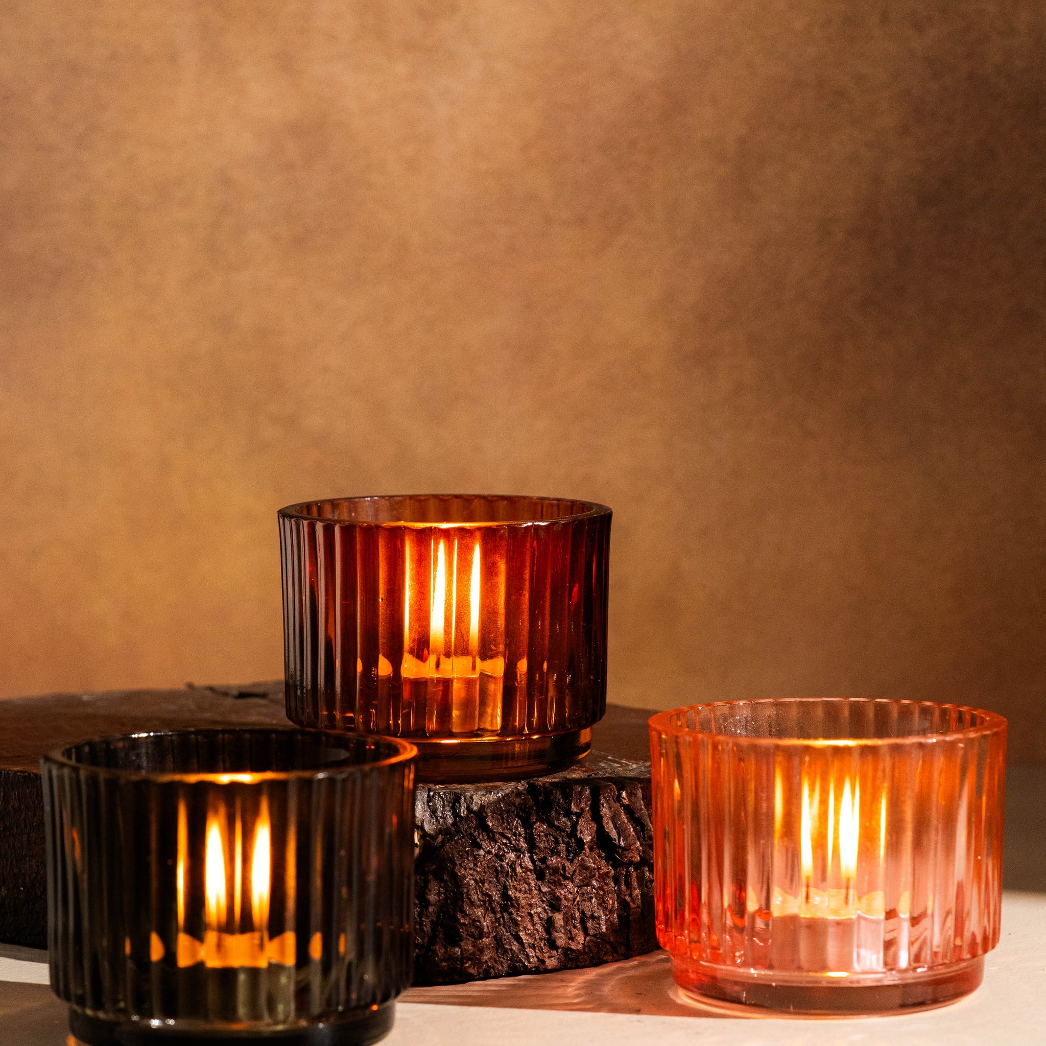 Three glass candle holders with candles on a textured surface and brown background