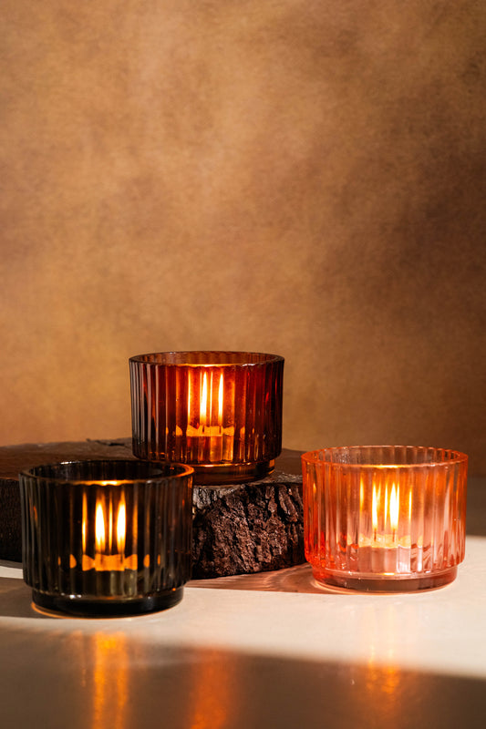 Three glass candle holders with candles on a textured surface and brown background