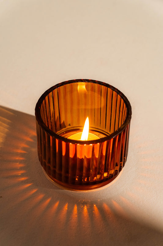 Amber glass candle holder with a lit candle on a neutral background
